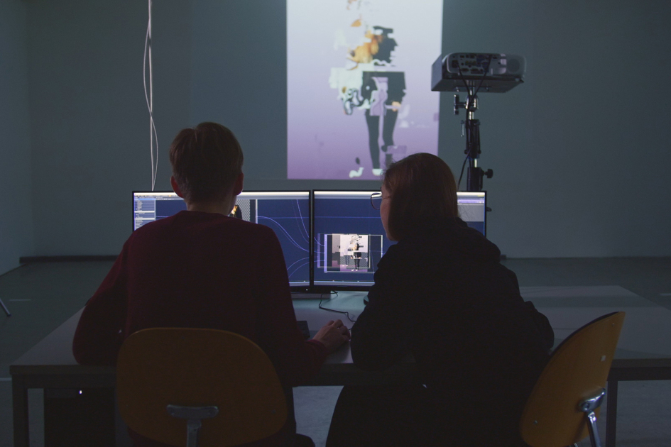 Zwei Personen arbeiten an einem PC, der im Hintergrund mit einer Projektion verbunden ist