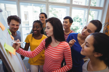 Viele Personen stehen um ein Flipchart herum und bearbeiten zusammen eine Aufgabe