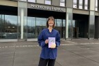 Carina Thomas steht mit ihrem Buch vor der Hochschule Bielefeld und lächelt