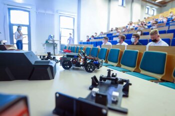 Ein unverkleidetes ferngesteuertes Auto und weitere Einzelteile liegen auf einem Tisch im Hörsaal