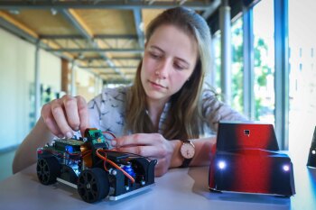 Eine Studentin verkabelt ein ferngesteuertes Auto neben einem weiteren bereits verkleideten Auto