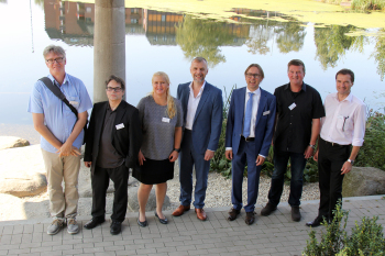 Sieben Mitwirkende des Symposium Energiekonzepte-Sennestadt stehen vor dem See am Sennestadthaus