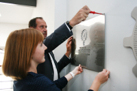 Ein Mann und eine Frau befestigen ein silbernes Schild an eine Wand.