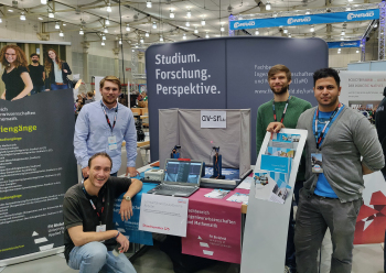 Vier Männer vor einem Messestand in einer Halle