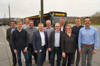 Elf Personen stehen vor einem Bus und blicken in die Kamera.