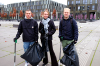 Tobias Franke, Melanie Vormwald und Luis Beumer-Scheidsteger stehen mit Greifzangen und Müllbeuteln in der Hand auf dem FH-Vorplatz