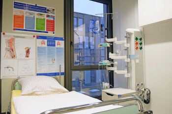 Ein Krankenhausbett steht in einem Raum mit Fenster, daneben steht ein Ständer, an dem Medikamente angebracht werden können.