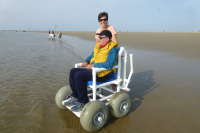 Ein Mann sitzt in einem Strandmobil, eine Frau steht dahinter