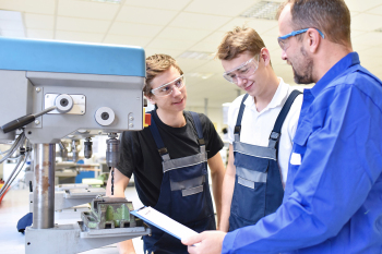 Drei Personen stehen in einer Fabrikhalle an einer Maschine im Gespräch