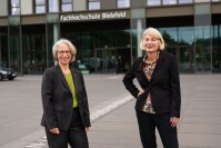 Zwei Frauen stehen vor dem Gebäude der Fachhochschule Bielefeld und lächeln in die Kamera.