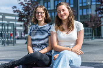 Cara Schmid und Viktoria Rekowski sitzen auf einem Enzi vor dem Hauptgebäude