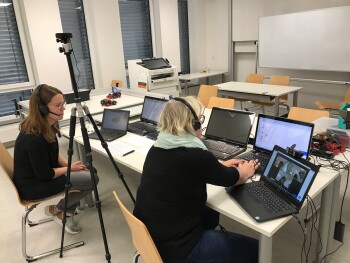 Zwei Frauen sitzen an einem Tisch und arbeiten an mehreren Laptops.