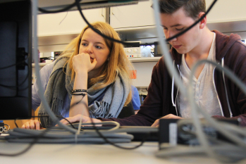 Mädchen und Junge sitzen vorm Bildschirm eines Computers.