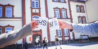 Zwei Tassen mit neuem HSBI Logo vor dem Gebäude des Campus Minden^