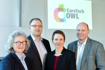 Zwei Frauen und zwei Männer stehen vor einer Wand, im Hintergrund ist das Logo von CareTech OWL zu sehen