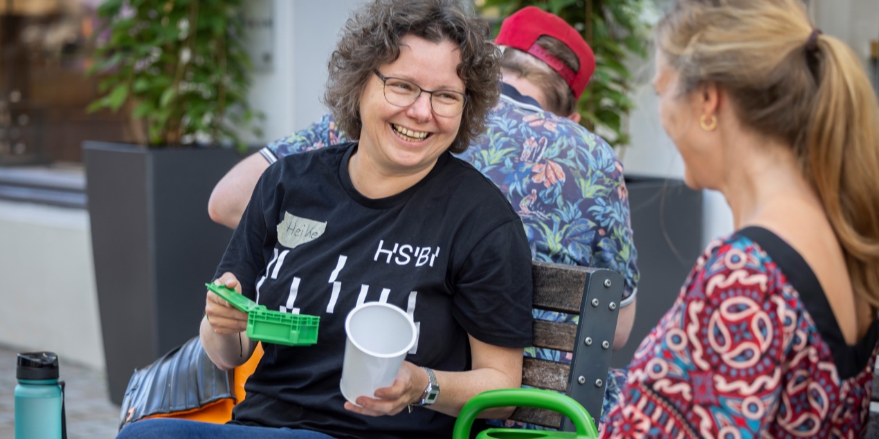 Heike Wulf die die Science Bench Aktion als Wissenschaftlerin betreut sitzt auf einer Bank in der Rathausstraße und unterhält sich mit einer Frau