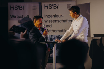 Vizepräsident Anant Patel und Ben Hartwig von den Stereotypen stehen während ihres Auftritts beim Demo Day vor einem Stehtisch und führen ein Interview