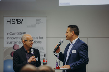 Ingo Ballschmieter und Armando Garcia Schmidt stehen während ihres Vortrags beim Demo Day an einem Stehtisch und halten Mikrofone in der Hand