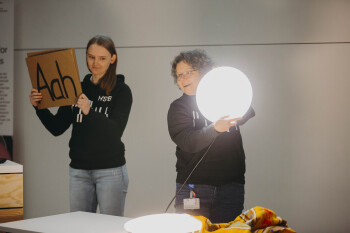 Bild von Katharina Schnatmann und Heike Wulf die beide in schwarzen Kapuzenpullovern auf der Bühne stehen Schnatmann hält ein Schild mit der Aufschrift Aah hoch wulf eine leuchtende Wandlampe