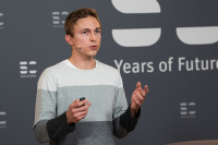 Fabian Schoden steht vor einer Wand mit dem 50 Years of Future Logo und spricht in eine Kamera