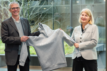 Ein Mann und eine Frau halten einen grauen Hoodie mit der Aufschrift FH Bielefeld hoch