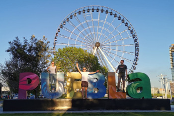 Drei Personen stehen vor einem großen Schild, auf dem Puebla steht. Im Hintegrund ist ein Riesenrad zu sehen.