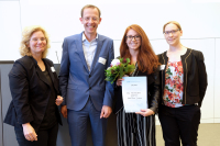 Drei Frauen und ein Mann schauen in die Kamera, eine Frau hält einen Blumenstrauß und eine Urkunde in den Händen.