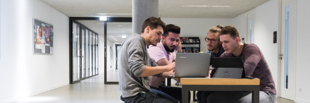 Vier Studenten sitzen mit ihren Laptops auf dem Gang im Lernbereich.