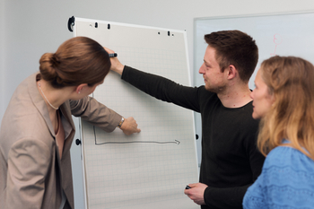 Drei Personen stehen an einem Flipchart und diskutieren