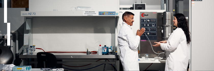 A guest researcher her host discuss a research topic in the lab