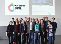 Eine Gruppe Menschen stehen vor einer Wand an die das Logo von CareTech OWL projiziert ist