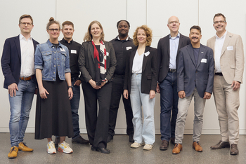 Nine people stand in front of a white wall