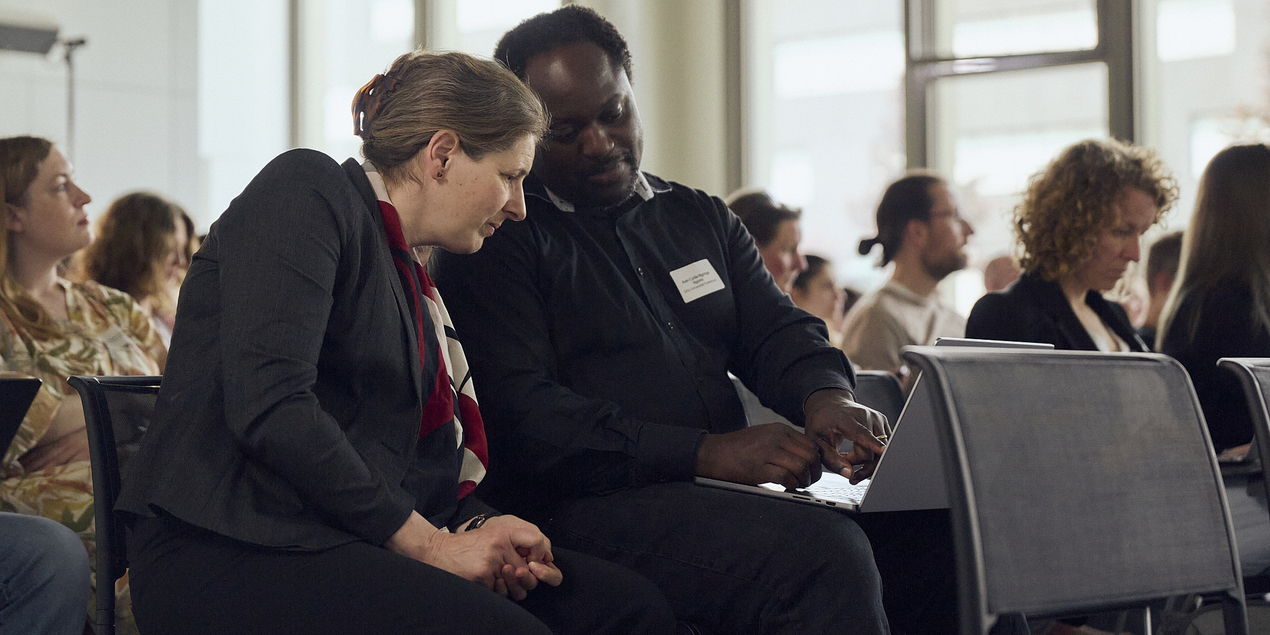 Barbara Hammer and Axel-Cyrille Ngonga Ngomo watch something together on a laptop in the conference room