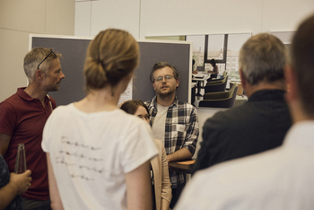 BIld einer Session des Bar Camps Acht Menschen stehen im Kreis vor einer grauen Pinnwand an der erste Ideen auf Karten geschrieben angepinnt sind