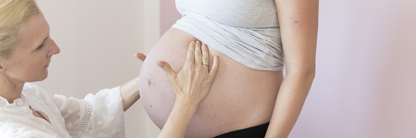 Eine Hebamme tastet den Bauch einer Schwangeren ab