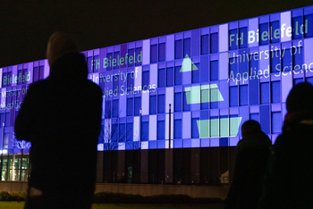 Zwei Personen stehen vor einem Gebäude, das Gebäude wird angestrahlt.