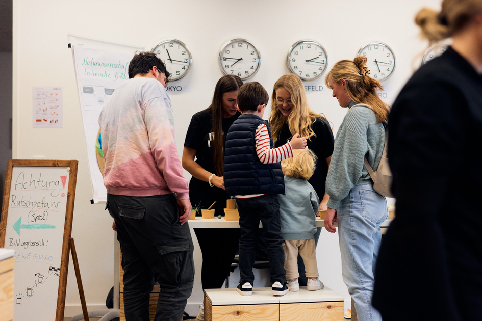 Eine Familie mit zwei kleinen Kindern spielt an einem Stand von Kindheitspädagogik