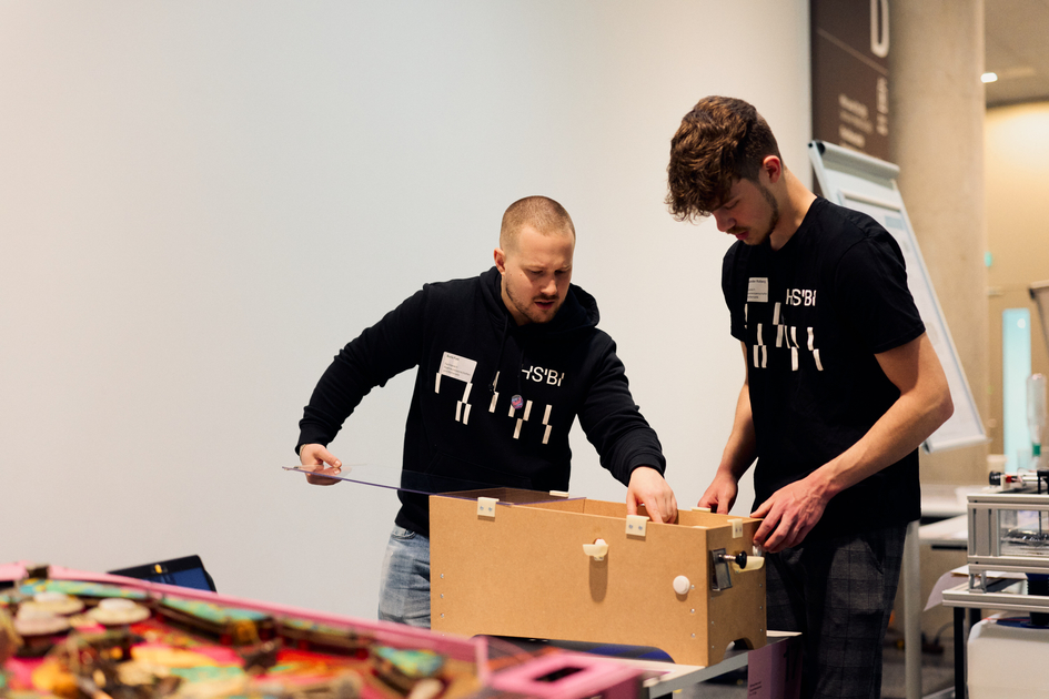 Zwei Studierende spielen an einer Flipper-Maschine