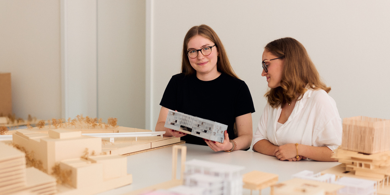 Zwei Studierende sitzen vor ihren Architekturmodellen