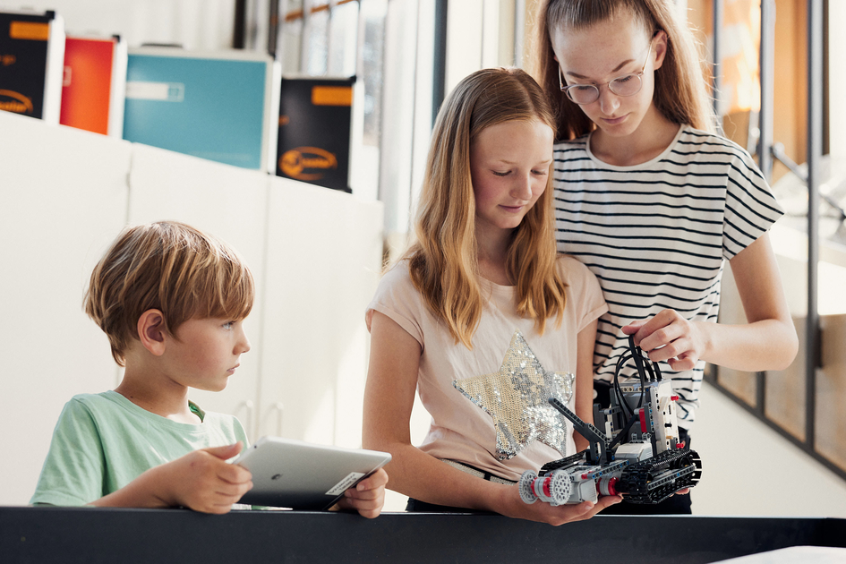 Drei Schüler*innen testen einen selbstgebauten Roboter.