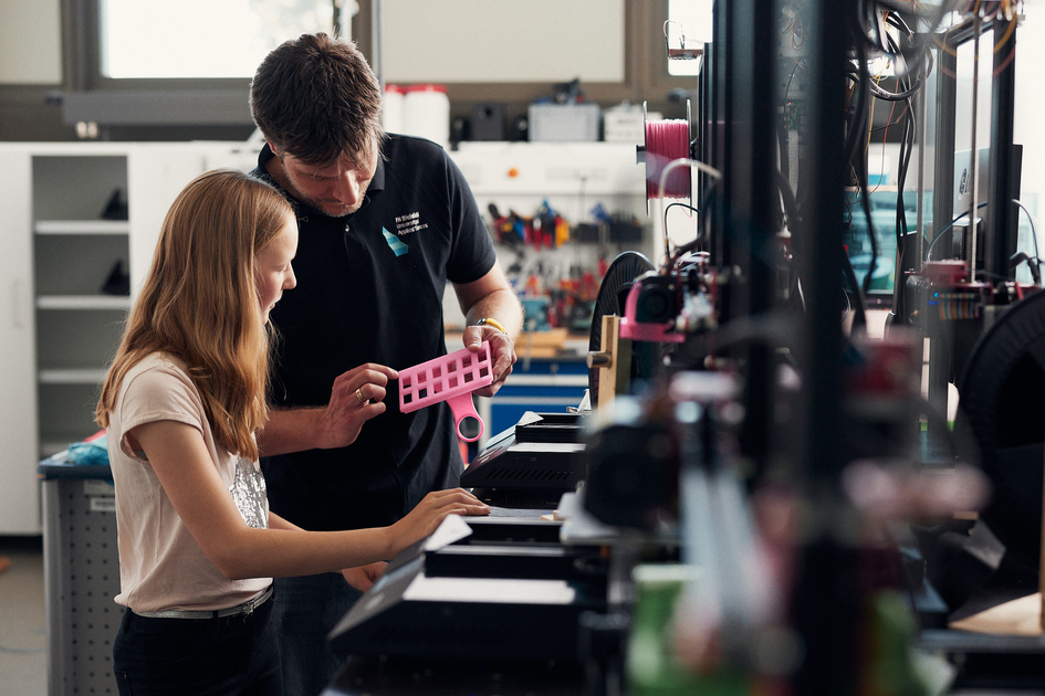 Ein Mann zeigt einer Schülerin ein Objekt aus einem 3D-Drucker