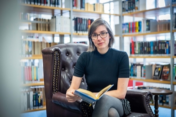 Sandra Holtgreve sitzt auf einem Sessel in der Bibliothek und hält ein Buch in der Hand