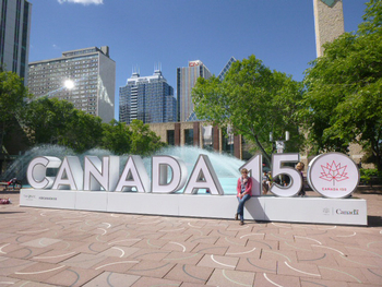 Eine Frau sitzt auf einem überdimensionalem Canada Schriftzug im Hintergrund eine Wasserfontäne