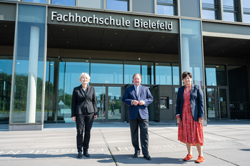 Zwei Frauen und ein Mann stehen vor dem Haupteingang der Fachhochschule Bielefeld