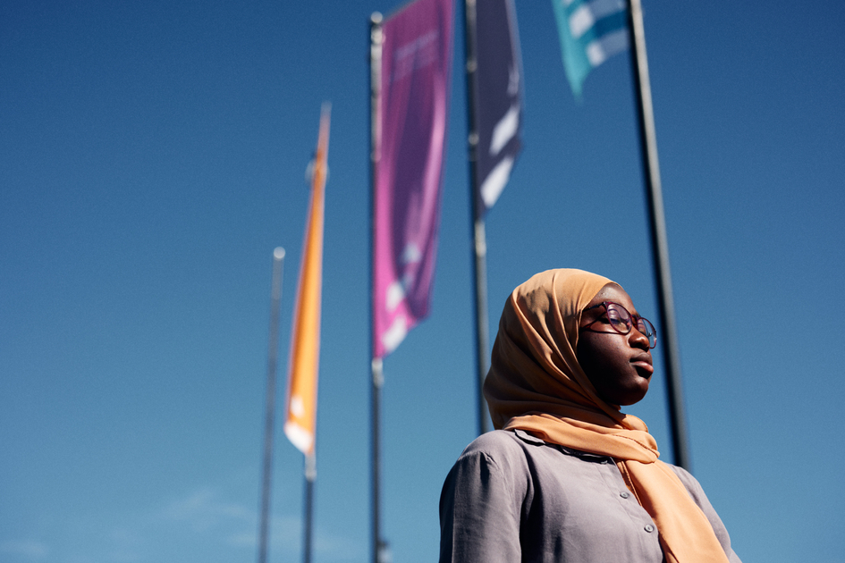 Hamdiya Alhassan steht vor den Flaggen der FH Bielefeld und leuchtend blauen Himmel