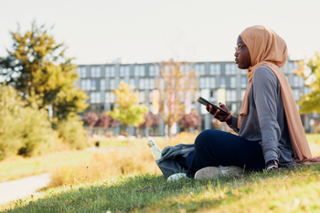 Hamdiya Alhassan sitzt auf einer Wiese vor dem Gebäude der FH Bielefeld