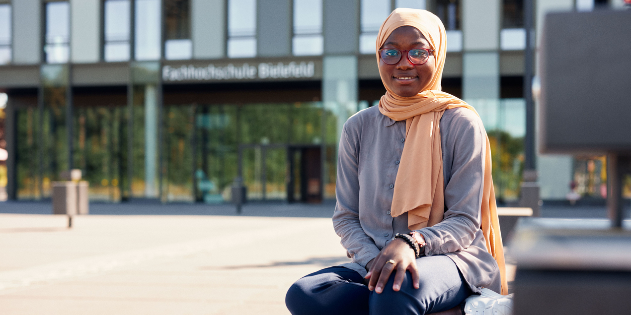 Hamdiya Alhassan sitzt auf einer Bank vor dem Haupteingang der FH Bielefeld