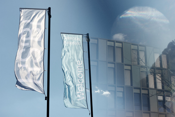 Two flags in front of the HSBI main building one with HSBI lettering one with Welcome lettering